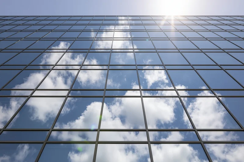 Glass curtain wall of modern office building reflecting blue sky and clouds
