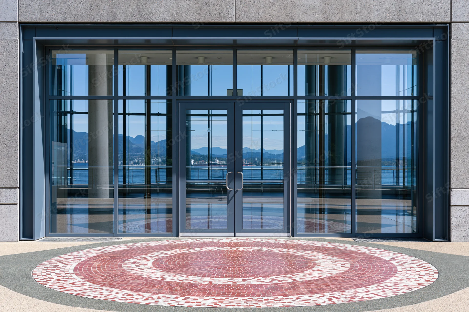 Glass double doors of a modern waterfront building entrance with mountain and water reflection in the glass