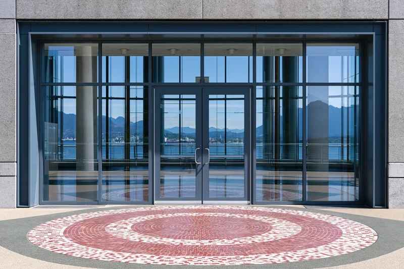Glass double doors of a modern waterfront building entrance with mountain and water reflection in the glass