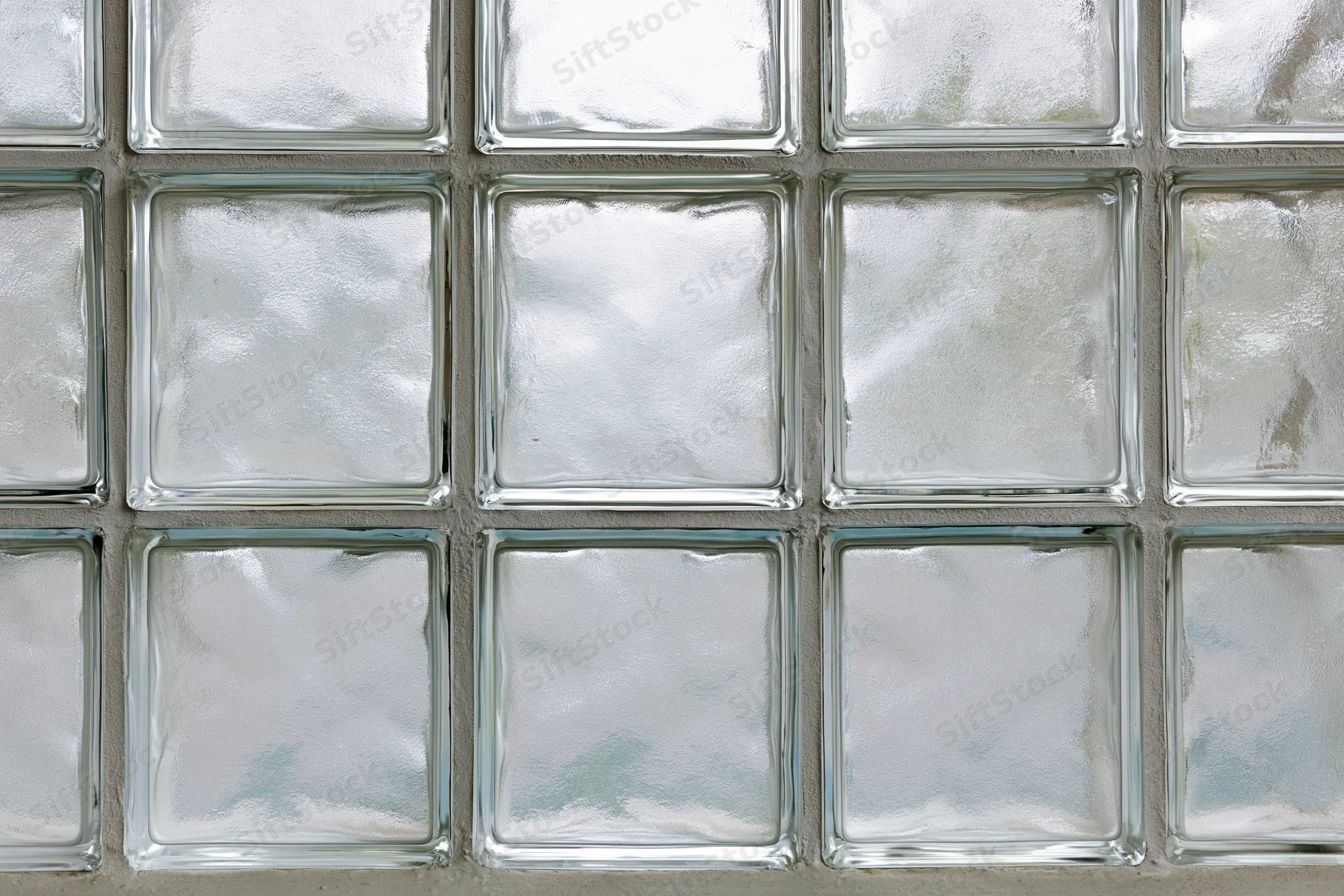 Grid of frosted glass blocks arranged in three rows with cement mortar joints on a wall