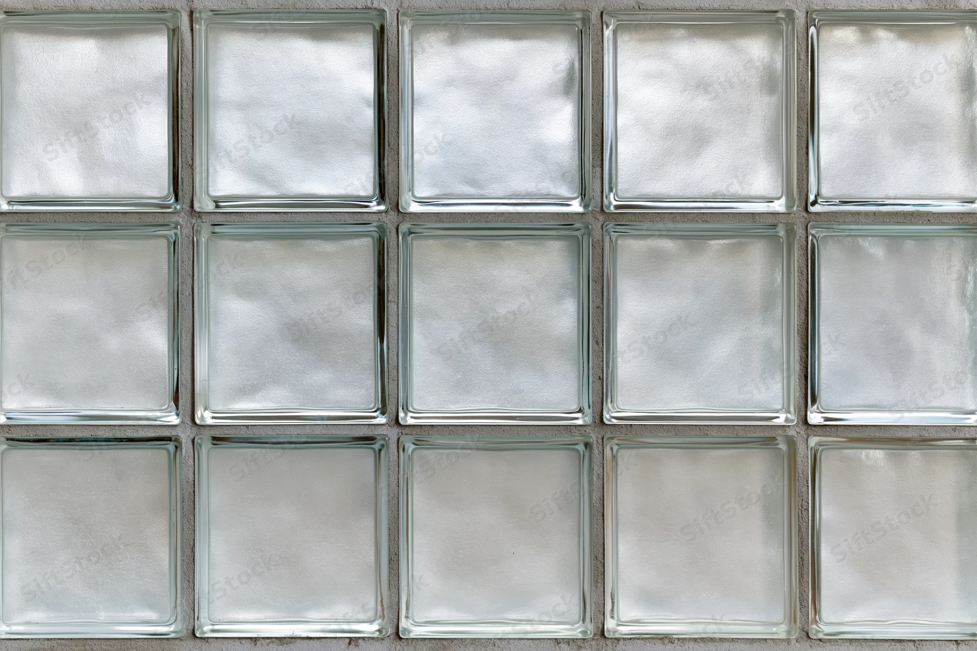 Grid of fifteen frosted glass block tiles arranged in three rows on a cement wall