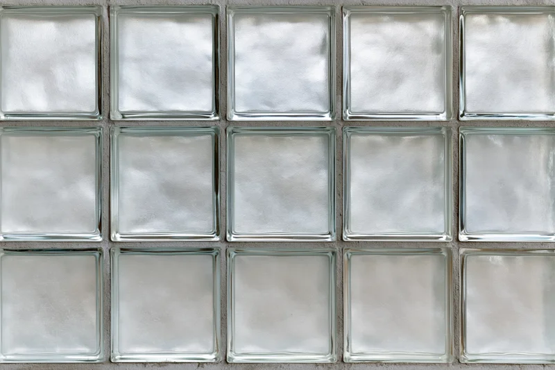 Grid of fifteen frosted glass block tiles arranged in three rows on a cement wall