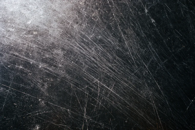 Heavily scratched black metal surface in close-up flat lay view