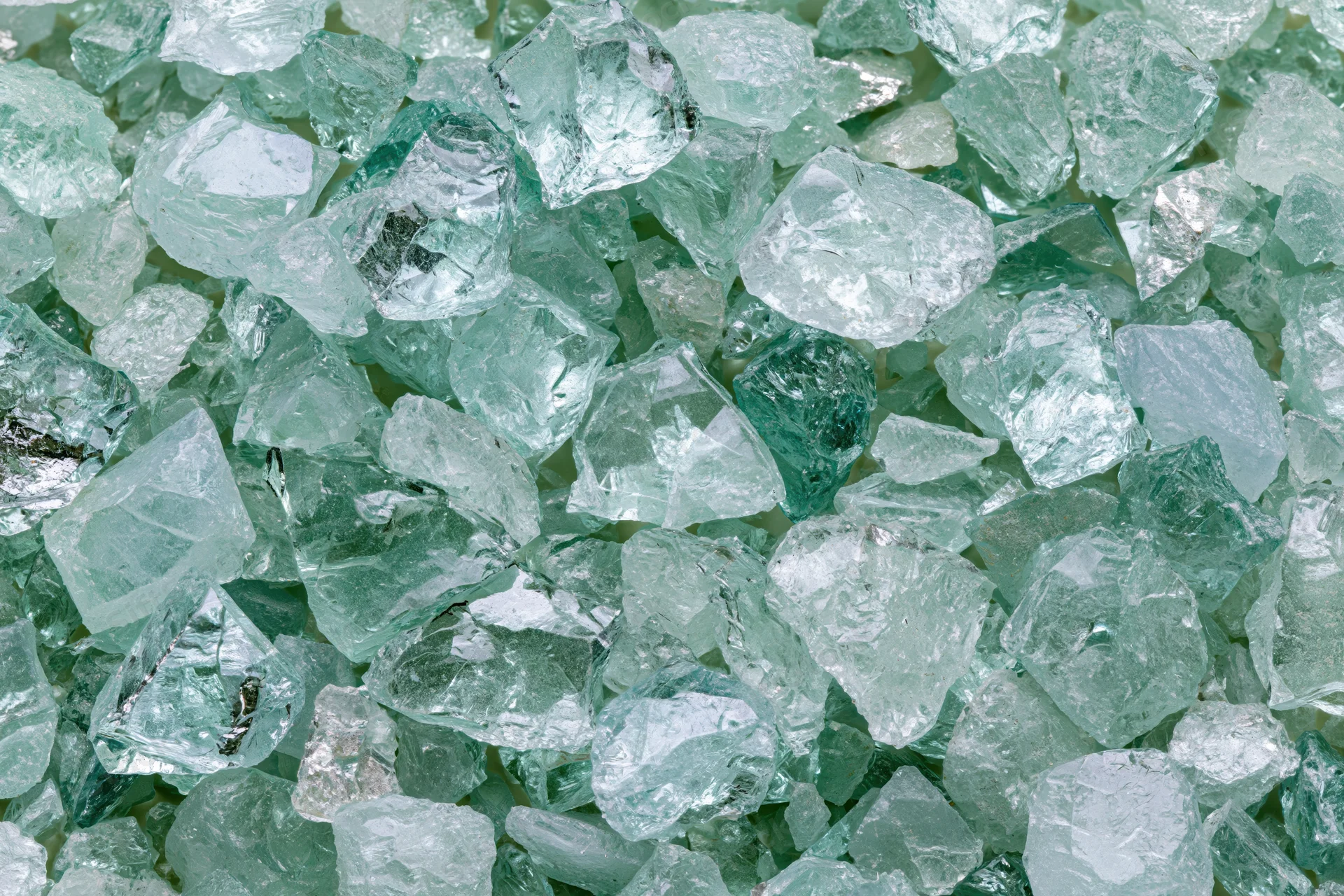 Crushed tempered glass fragments scattered densely in a pile, showing greenish transparent shards with rough edges and reflective surfaces