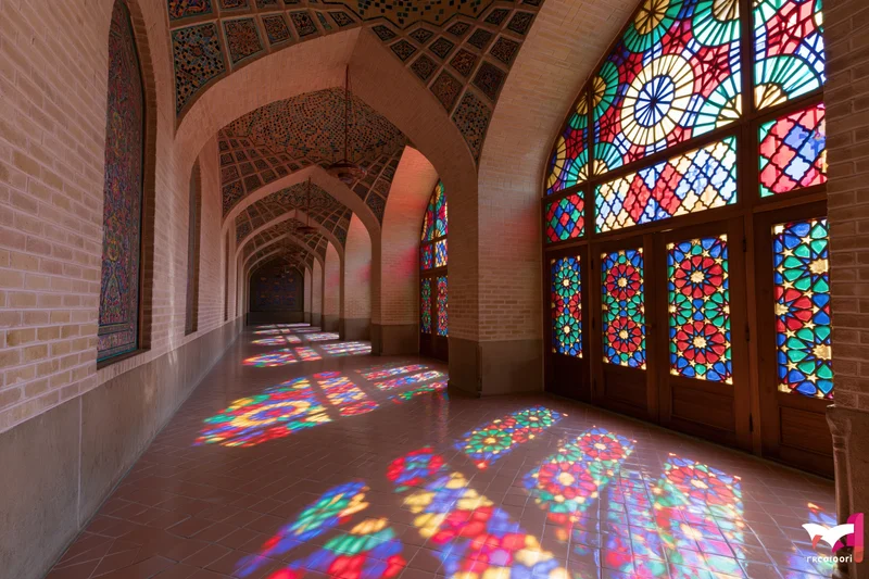 Interior of a historic iranian mosque with stained glass windows casting colorful light patterns on the tiled floor