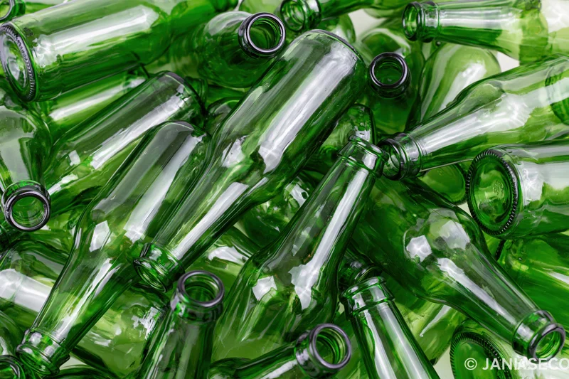 Pile of empty green glass beer bottles scattered and overlapping on a flat surface