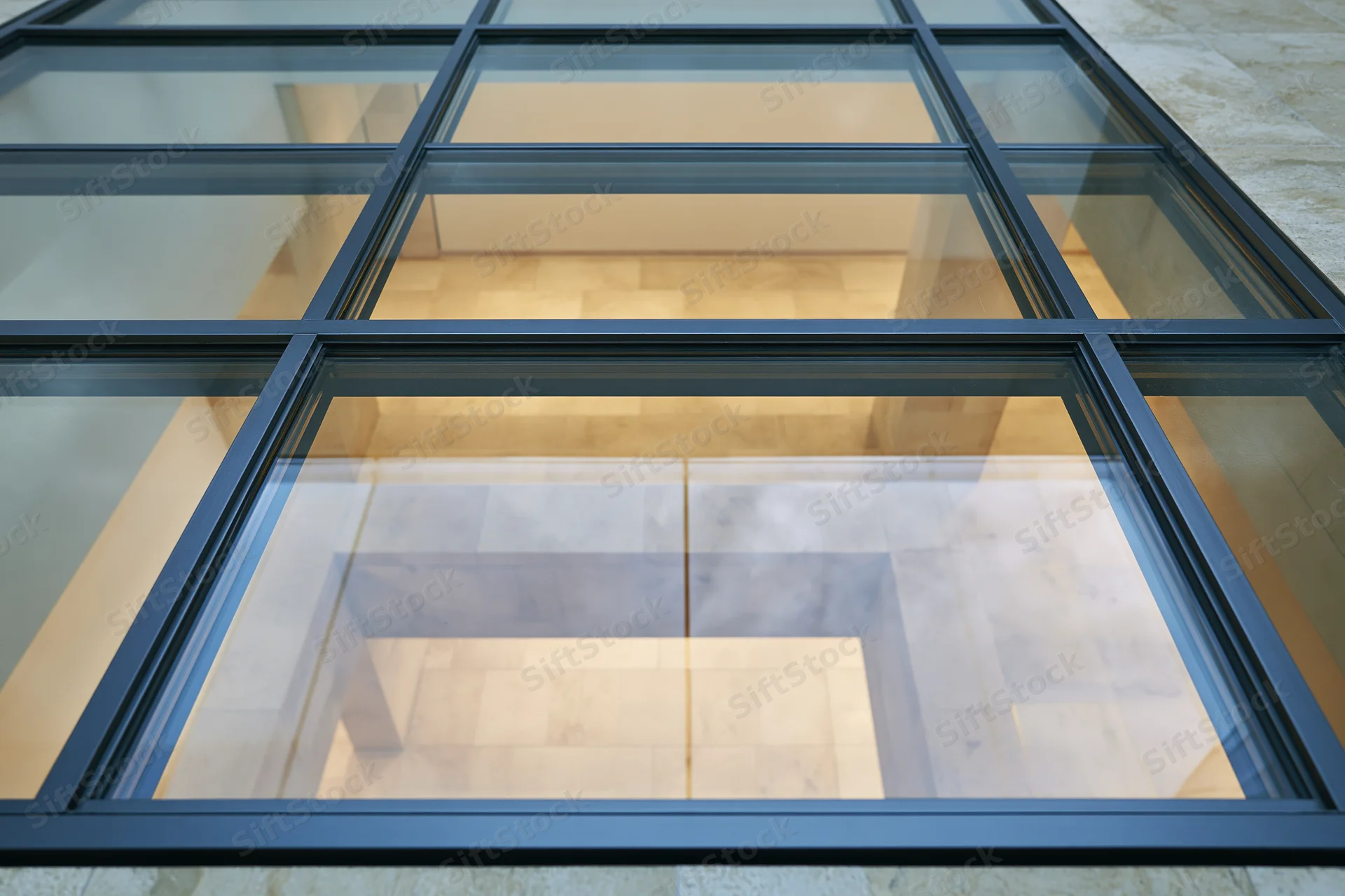Looking straight down through a structural glass floor panel into a tiled interior space