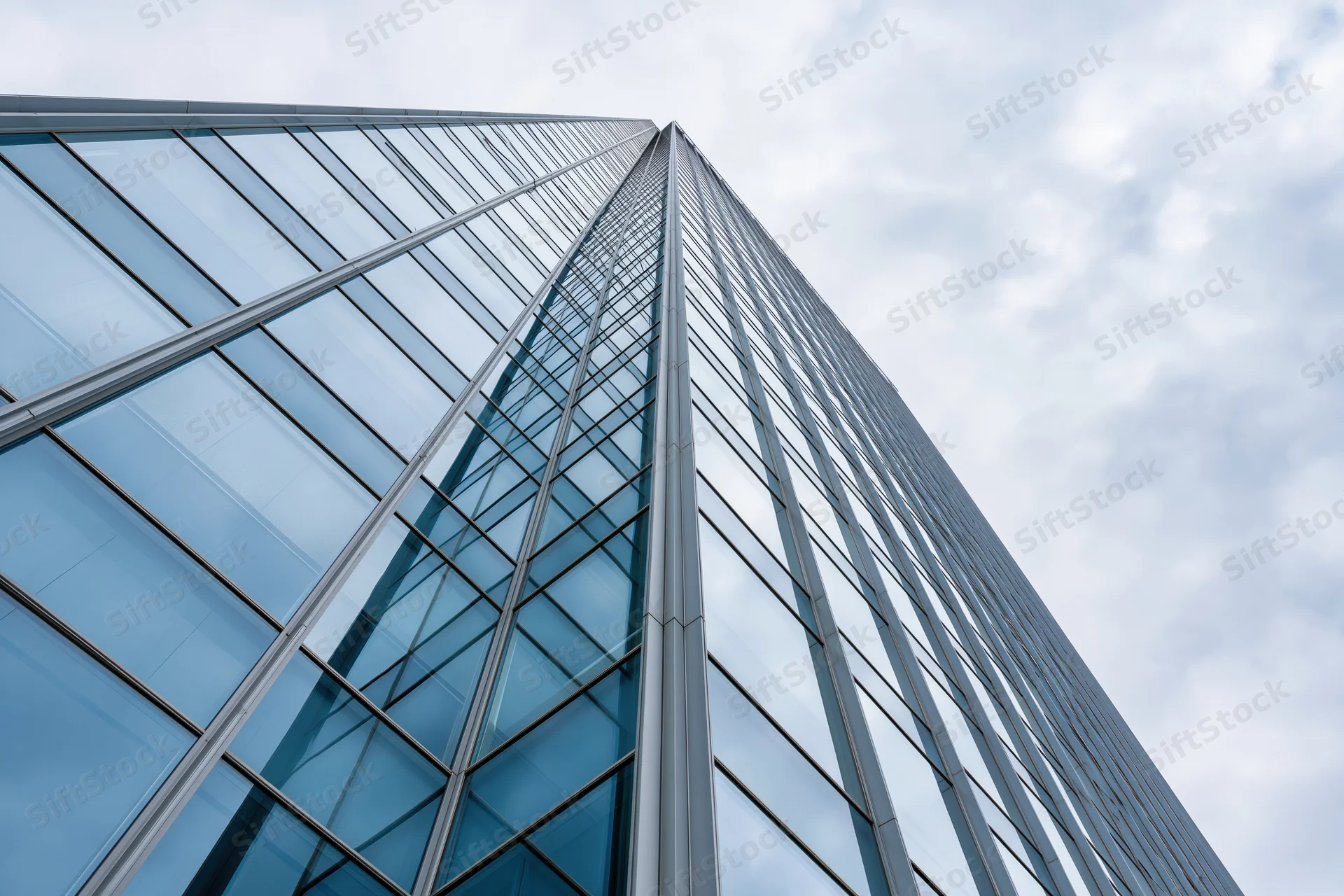 Modern glass curtain-wall skyscraper facade viewed from ground level against cloudy sky