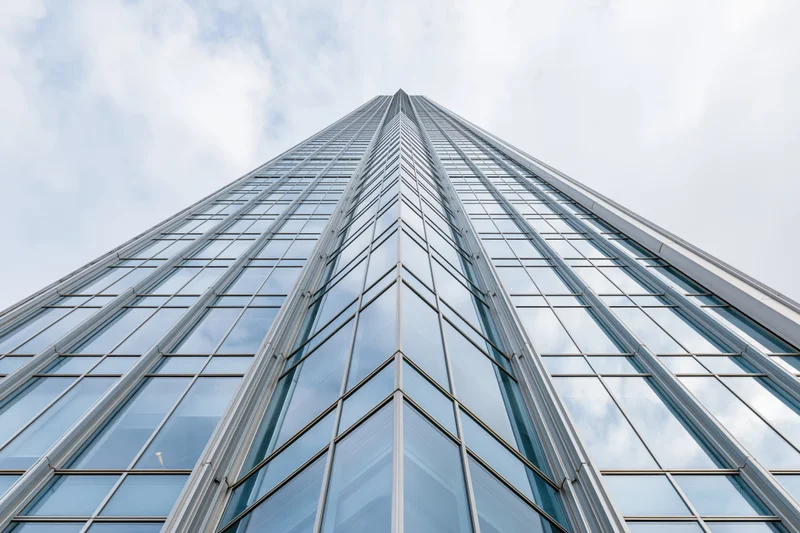 Modern glass curtain-wall skyscraper facade viewed from ground level looking upward