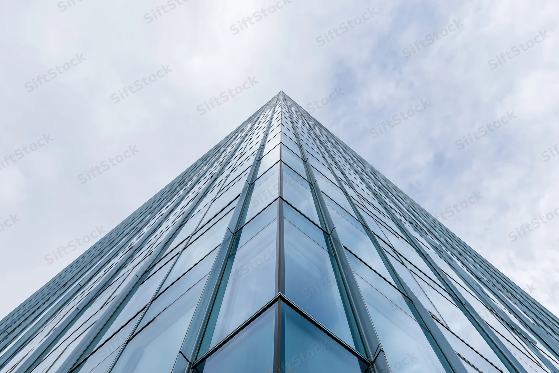 Modern glass curtain-wall skyscraper facade viewed from ground level against cloudy sky