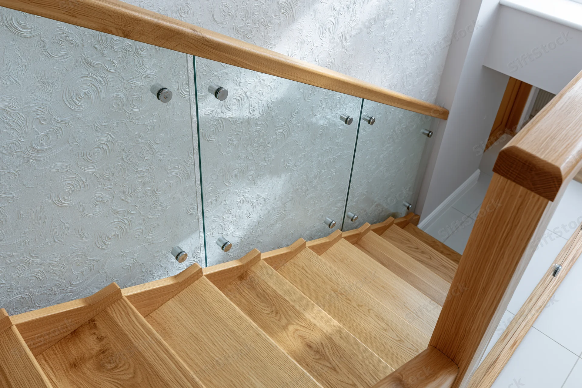 Modern interior staircase with light oak wood treads and glass railing in a residential hallway