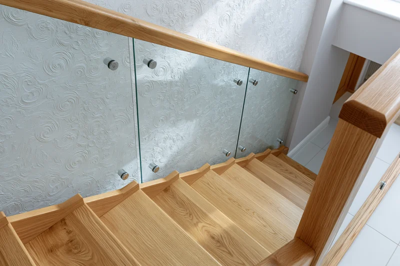 Modern interior staircase with light oak wood treads and glass railing in a residential hallway