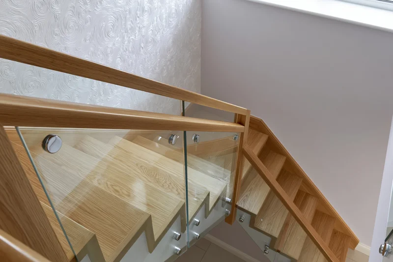 Modern interior staircase with light oak wood treads and glass railing in a residential home
