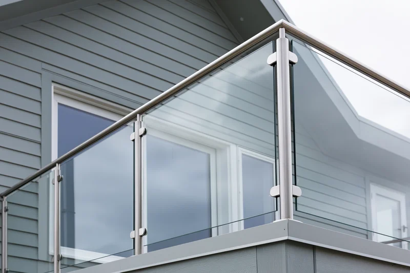 Frameless glass railing on a modern residential balcony with metal posts and gray siding