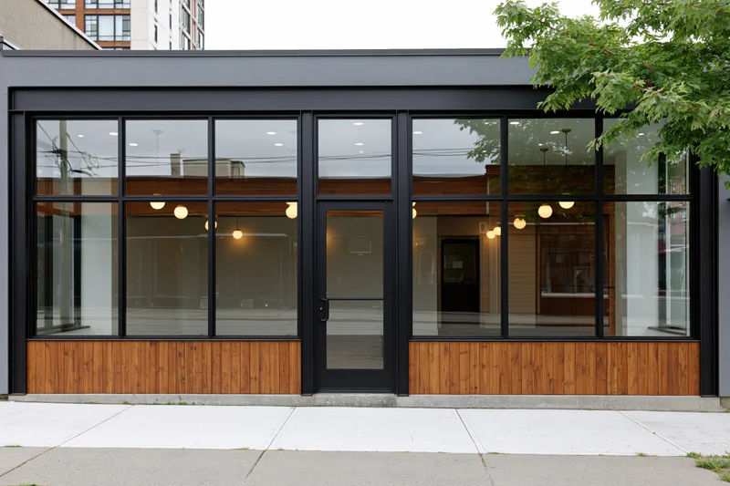 Modern retail storefront with large glass windows and wood paneling on sidewalk