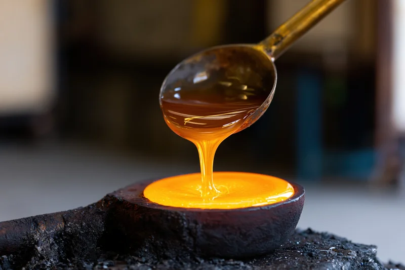 Molten glass pouring from a metal ladle onto a dark cast surface in a workshop