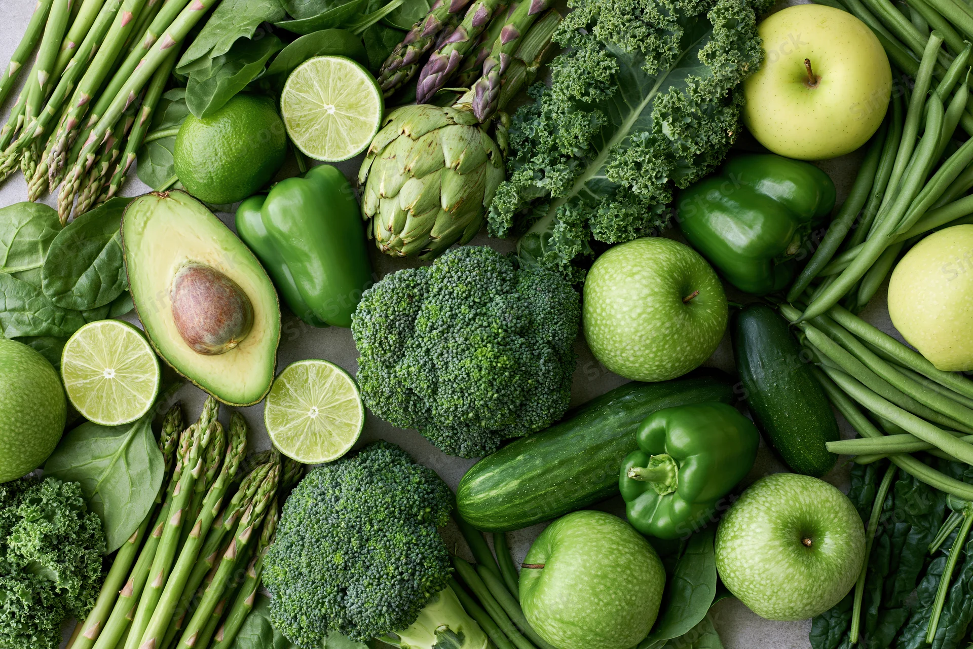 Overhead flat lay of assorted green vegetables and fruits arranged on a neutral surface