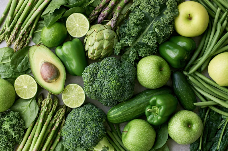 Overhead flat lay of assorted green vegetables and fruits arranged on a neutral surface