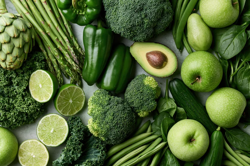 Overhead flat lay of assorted green vegetables and fruits arranged on a light surface