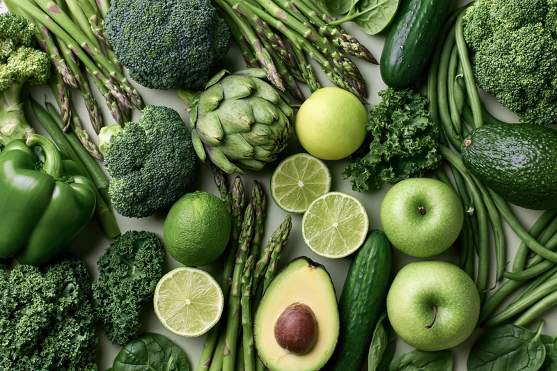 Overhead flat lay of assorted green vegetables and fruits arranged on a white surface