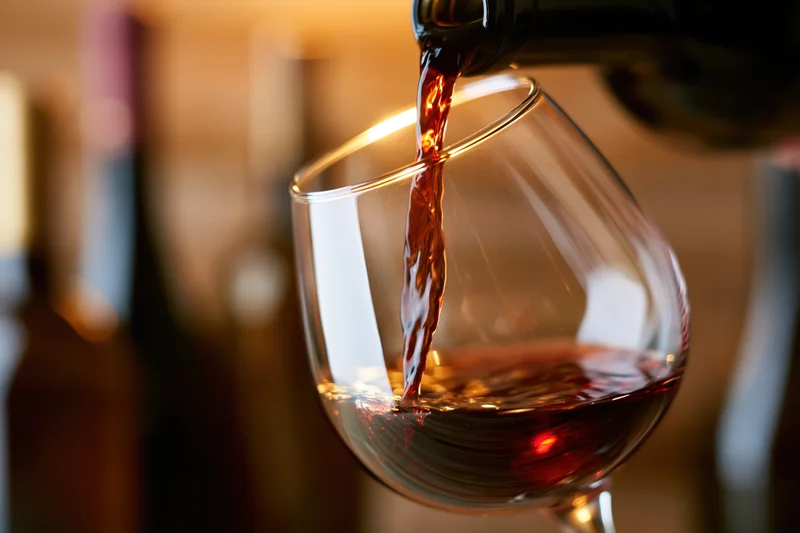 Red wine pouring from a dark bottle into a tilted crystal glass with blurred background