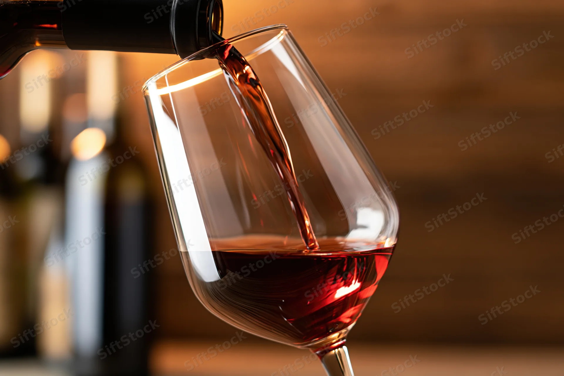 Red wine being poured from a dark bottle into a tilted crystal glass at a bar