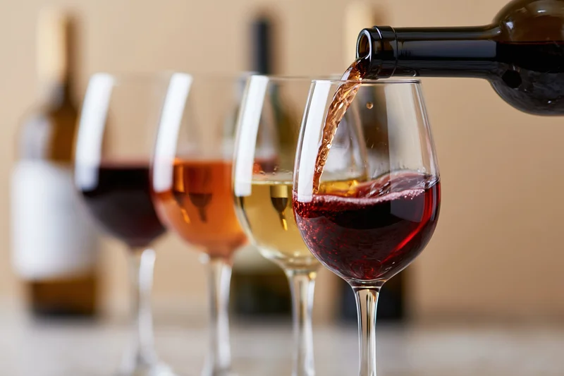 Red wine being poured from a dark bottle into the foremost of four glasses arranged in a row on a table