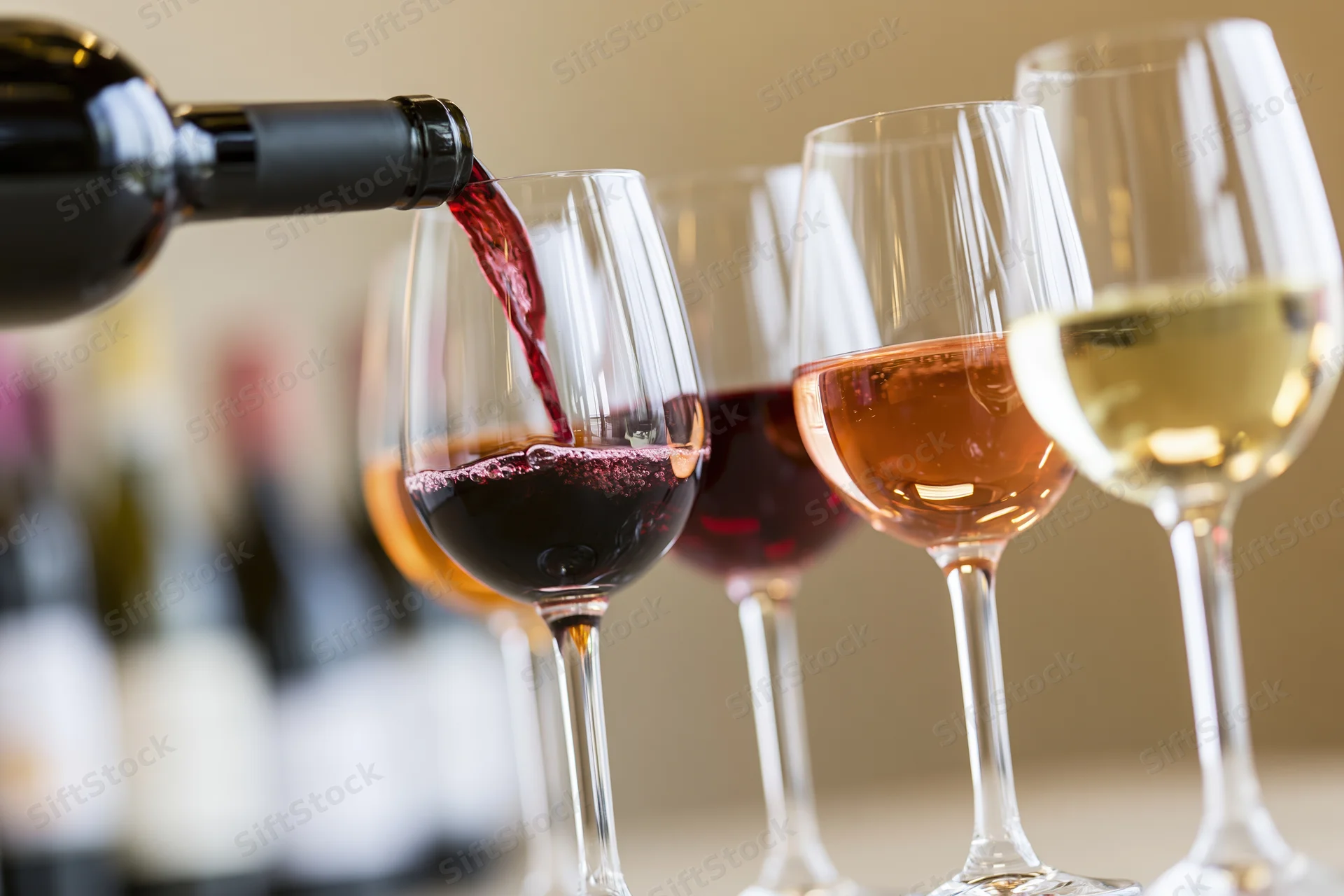 Red wine being poured from a dark bottle into a glass with other wine glasses in a row on a table