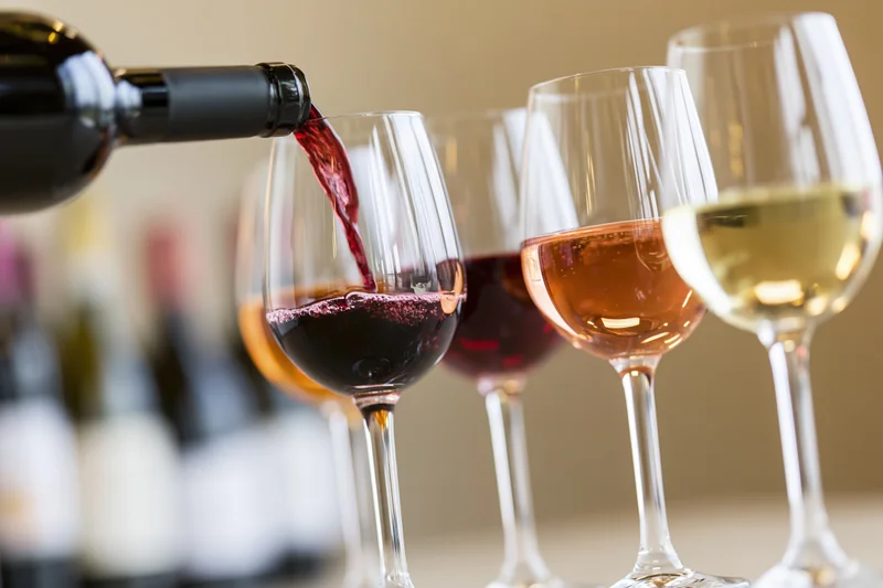 Red wine being poured from a dark bottle into a glass with other wine glasses in a row on a table