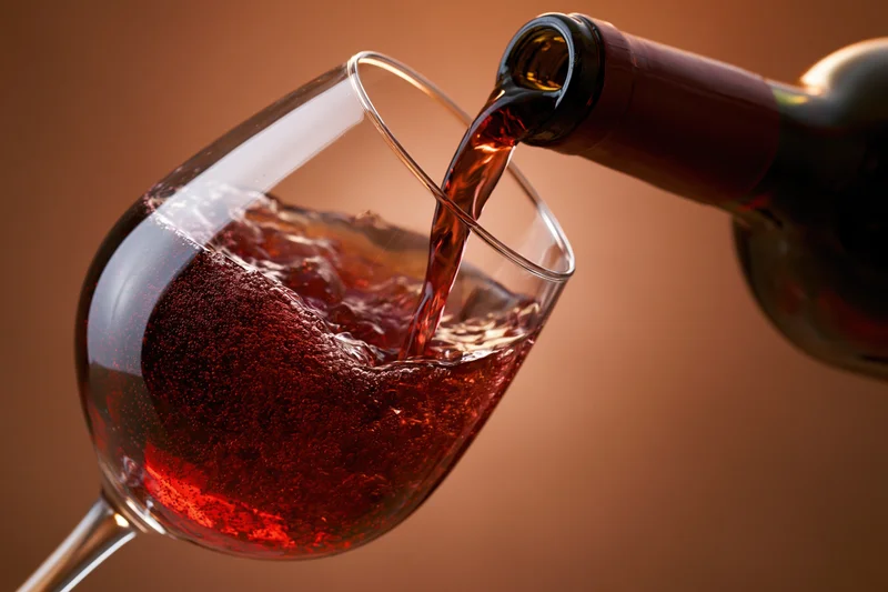 Red wine pouring from a dark bottle into a tilted crystal wine glass