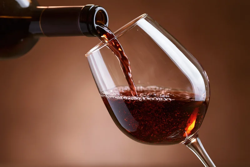 Red wine pouring from a dark bottle into a tilted crystal wine glass