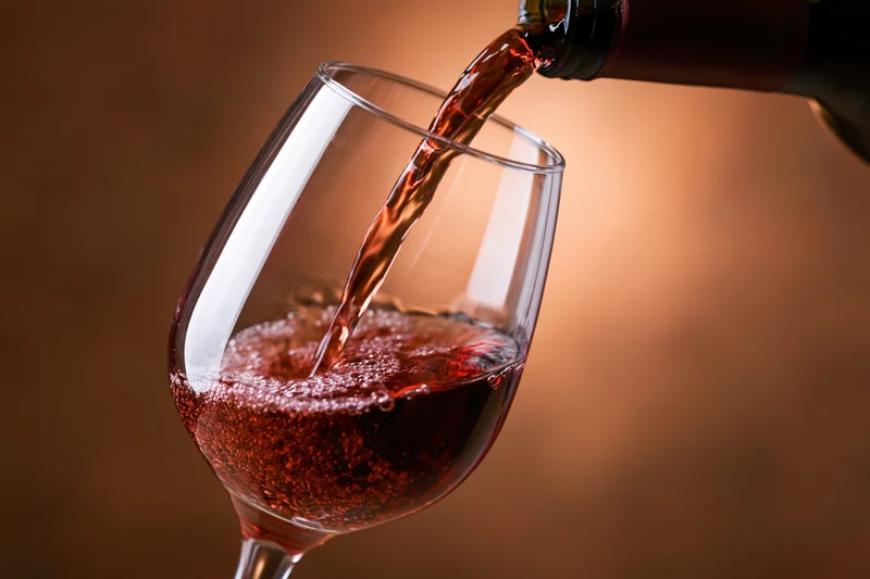 Red wine pouring from a dark bottle into a tilted crystal wine glass