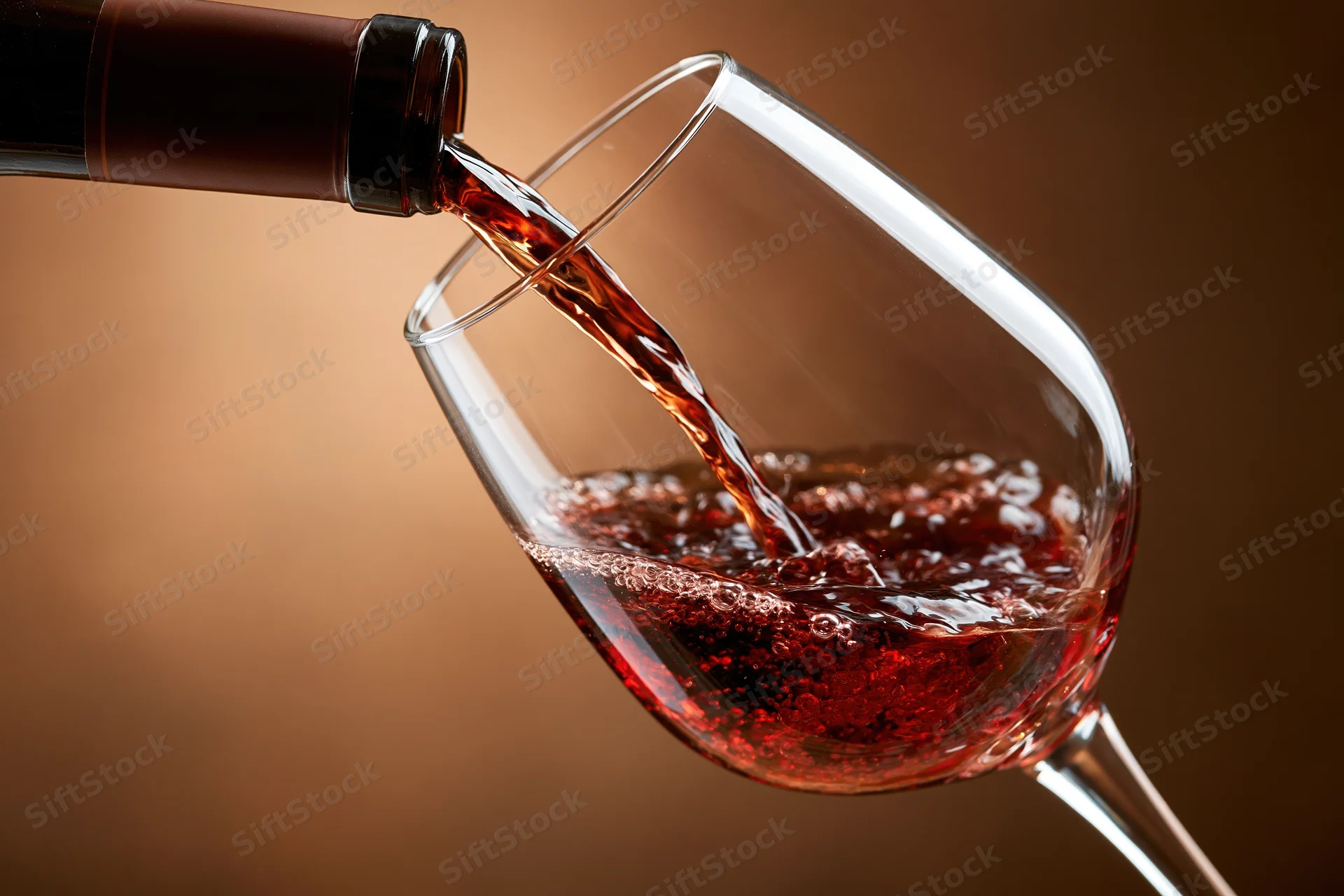 Red wine pouring from a dark bottle into a tilted crystal wine glass