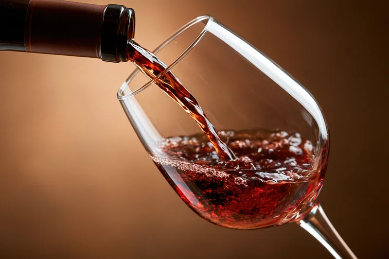 Red wine pouring from a dark bottle into a tilted crystal wine glass