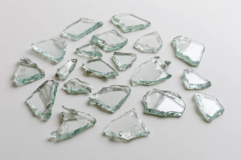Broken glass shards scattered on a plain white surface