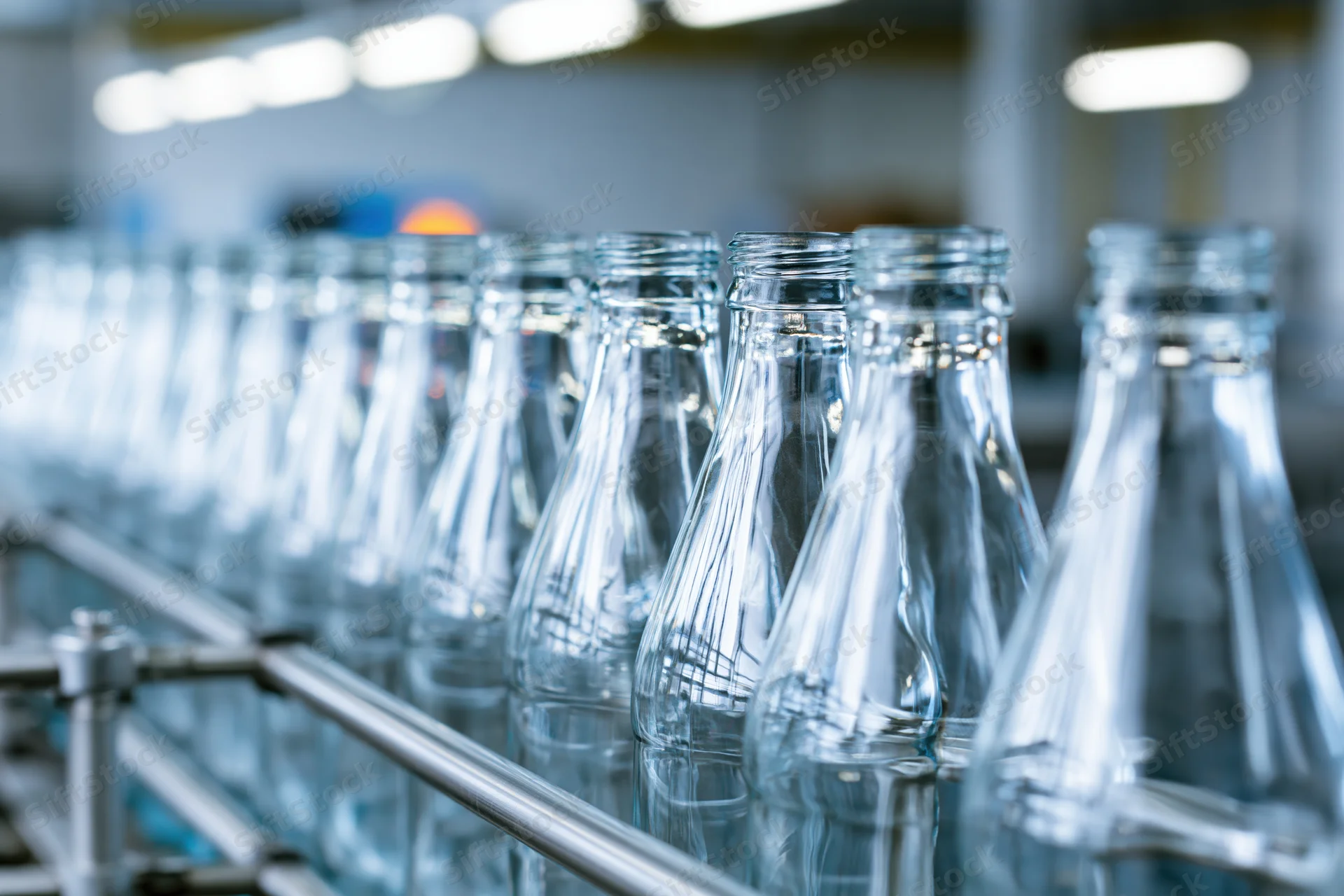 Empty clear glass bottles moving along a stainless steel conveyor in a factory production line