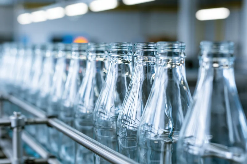 Empty clear glass bottles moving along a stainless steel conveyor in a factory production line