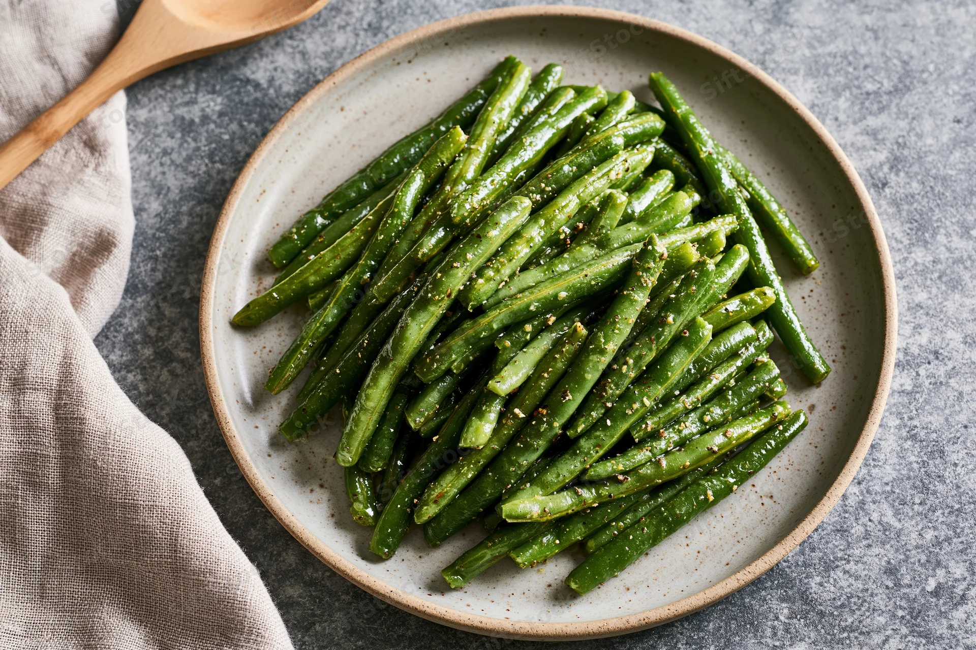 Sauteed green beans glistening with oil and spices piled on a ceramic plate