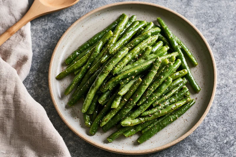 Sauteed green beans glistening with oil and spices piled on a ceramic plate