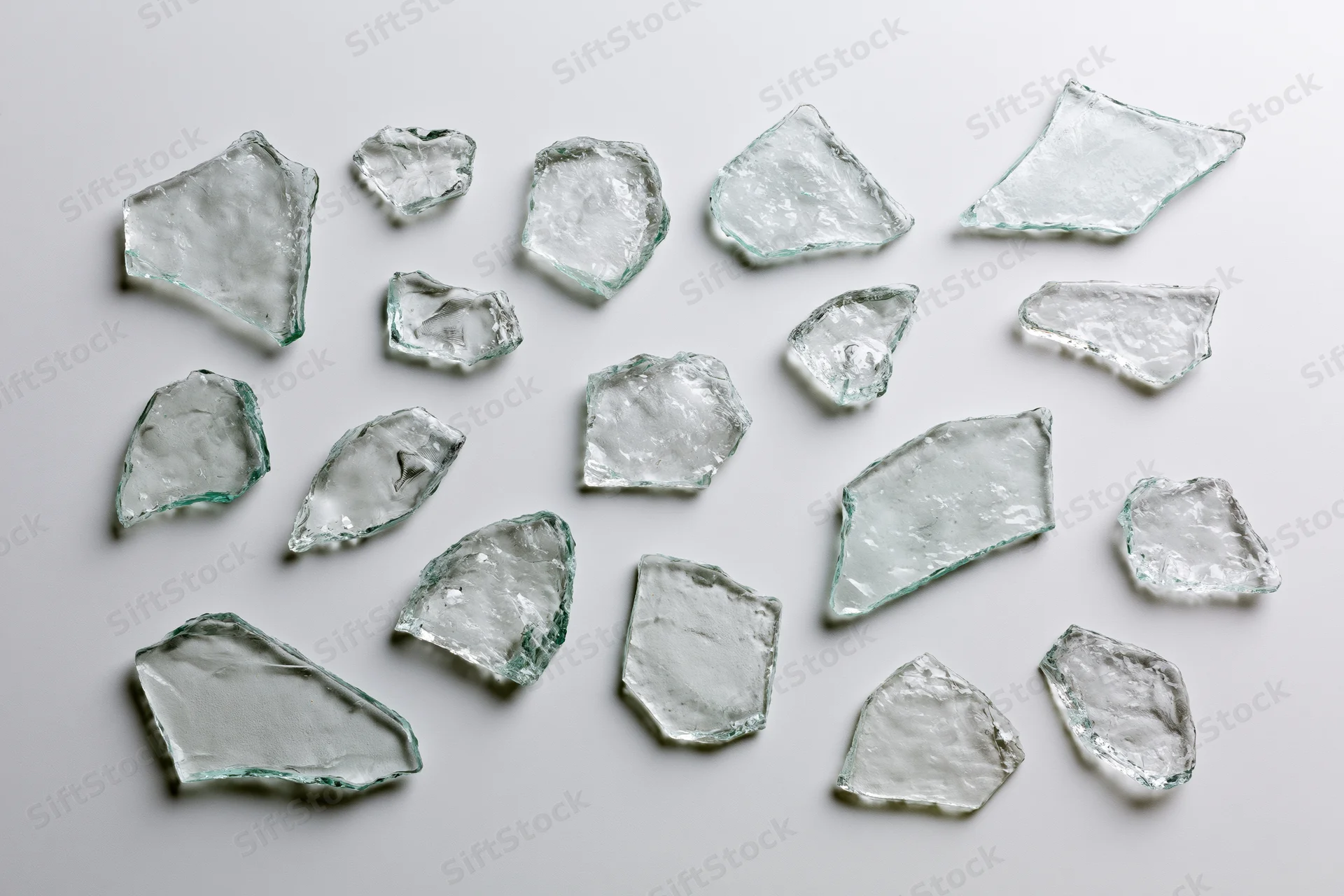 Scattered broken glass shards arranged flat on white surface