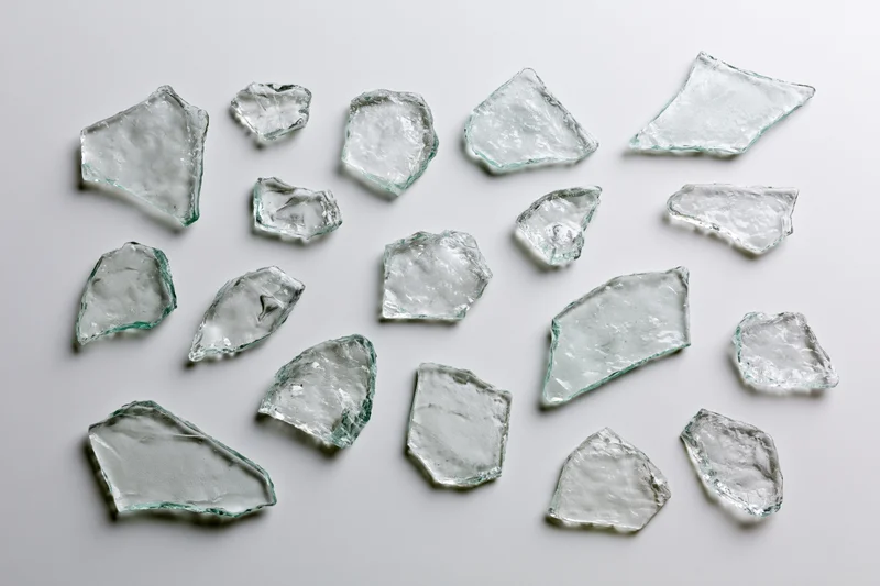 Scattered broken glass shards arranged flat on white surface
