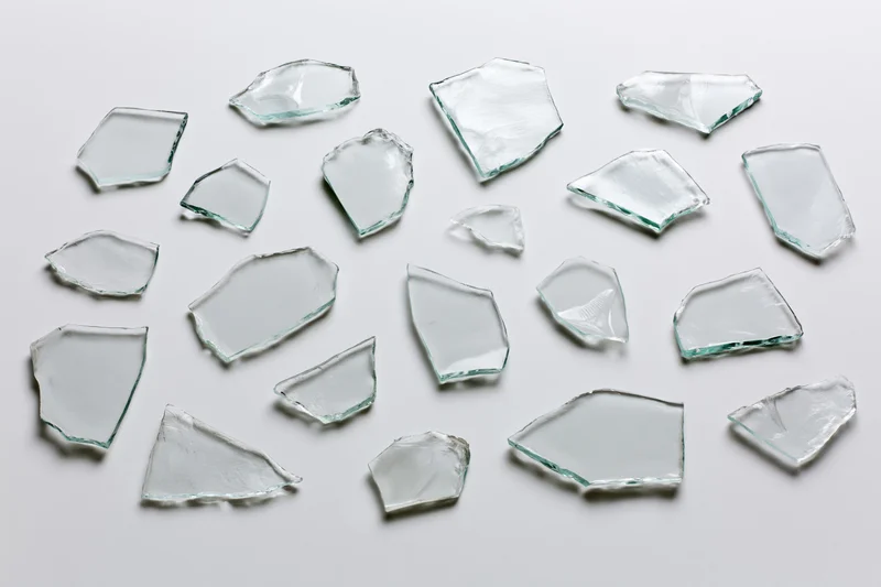 Scattered broken glass shards arranged flat on white surface