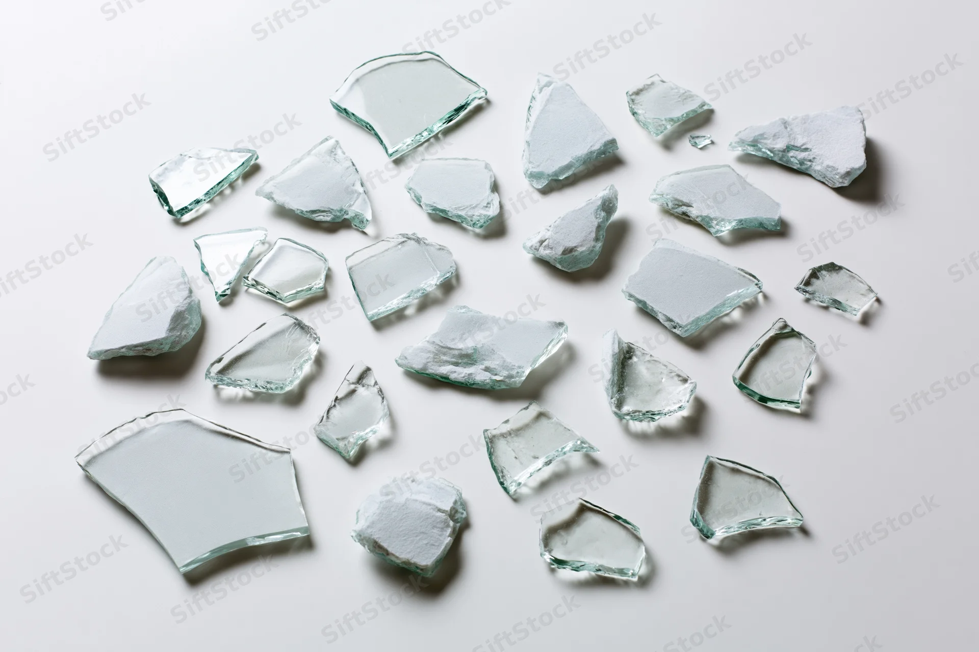 Scattered broken glass shards of various sizes arranged flat on white surface
