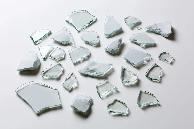 Scattered broken glass shards of various sizes arranged flat on white surface