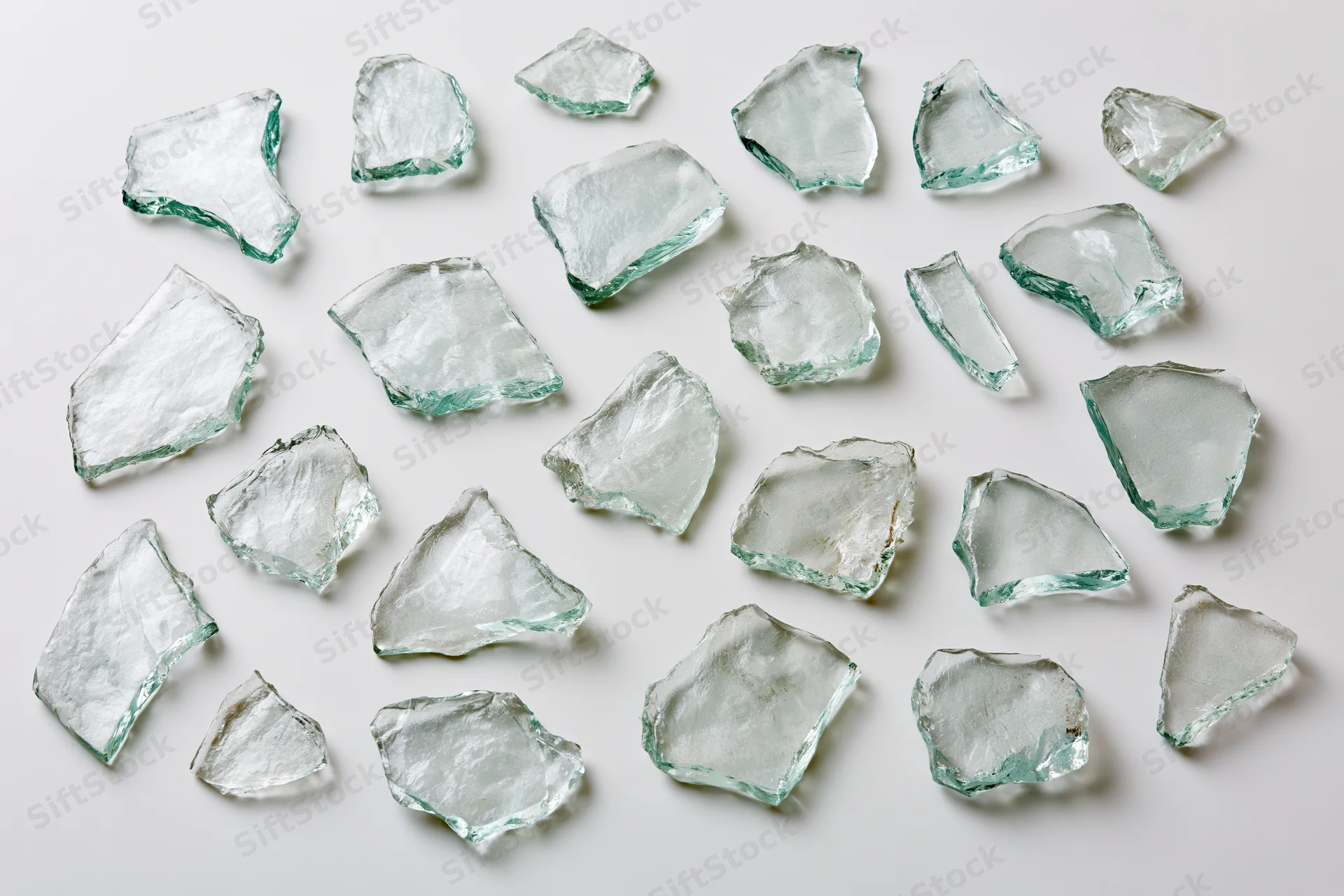 Scattered broken glass shards of various sizes arranged flat on white surface