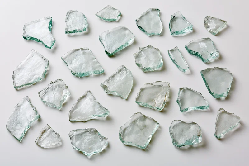 Scattered broken glass shards of various sizes arranged flat on white surface