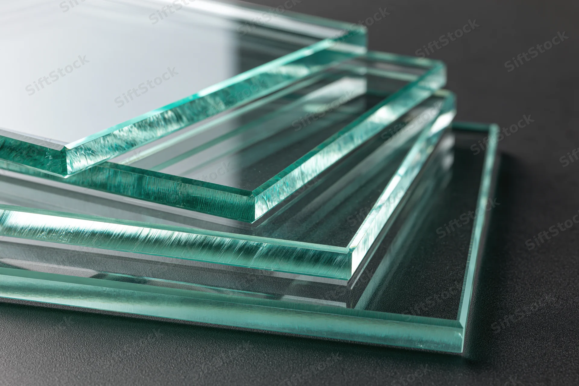 Flat glass panels stacked and fanned out on a dark surface