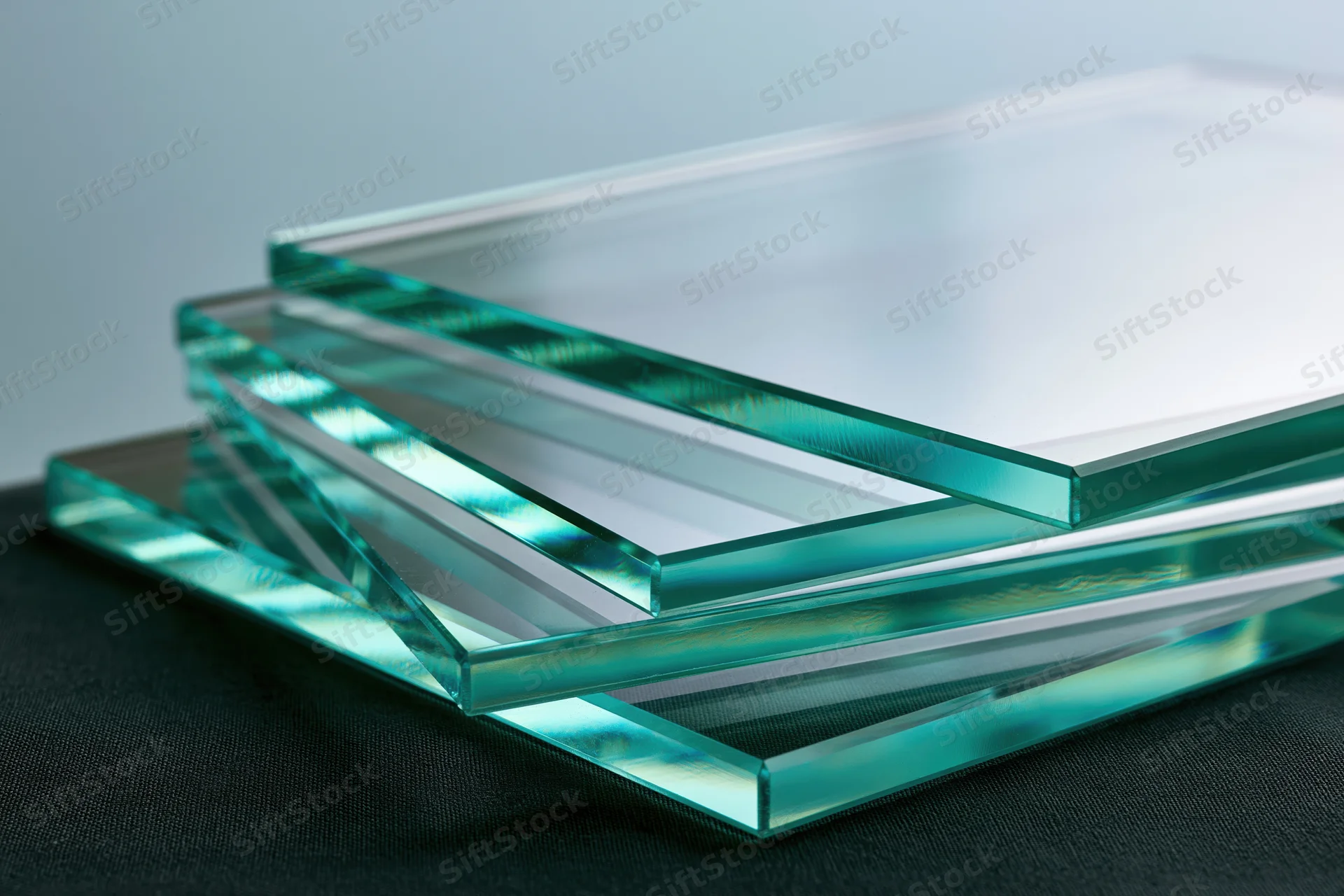 Cut glass sheets stacked and fanned out at angles on a dark surface