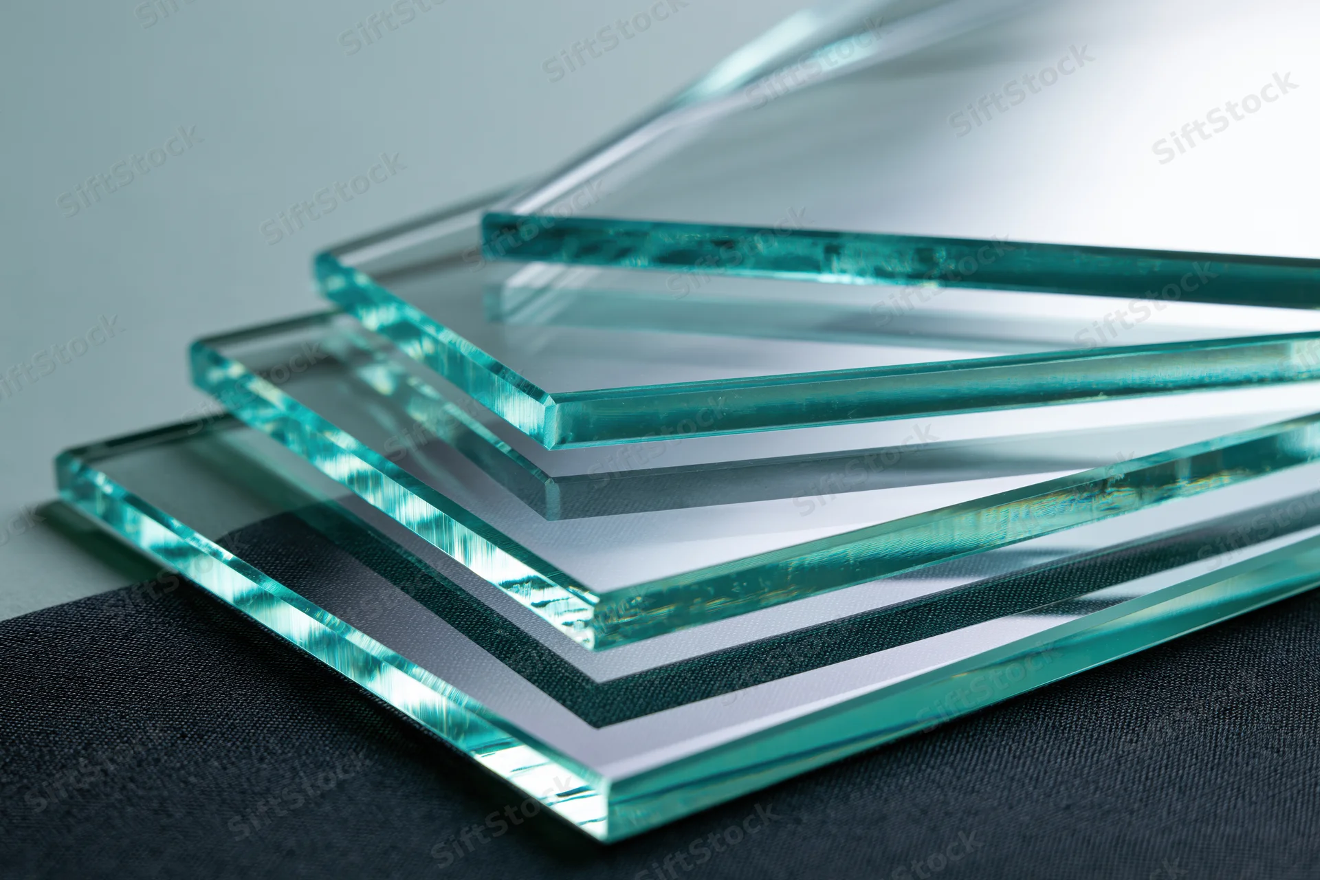 Cut glass sheets stacked and fanned out at angles on a dark surface