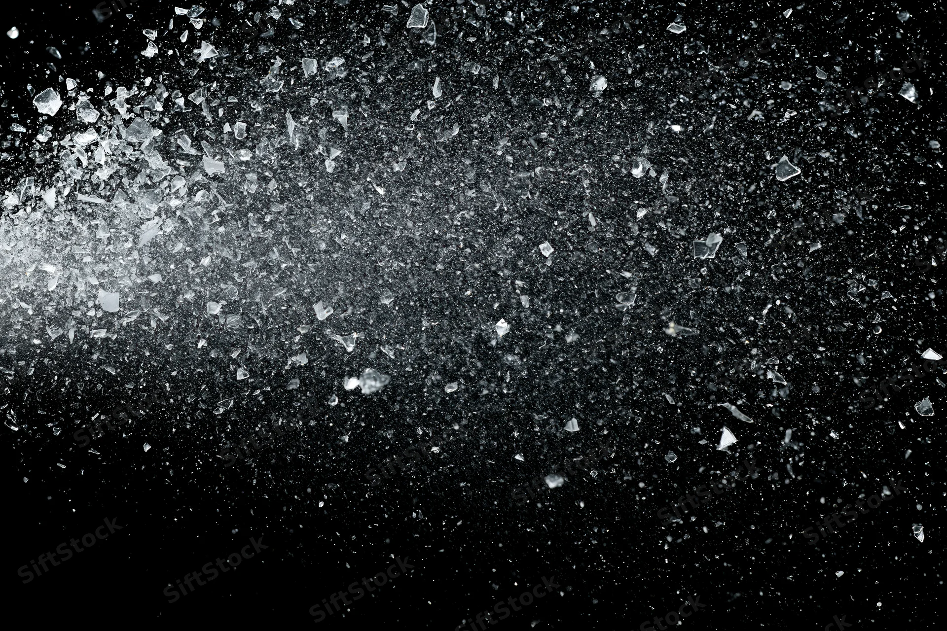 Shattered glass fragments and fine particles exploding outward against black background